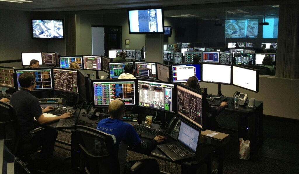 A bustling control room with people working on multiple computer monitors.