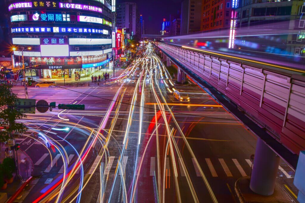 Dynamic city intersection with colorful light trails and neon lights at night, showcasing urban motion and energy.