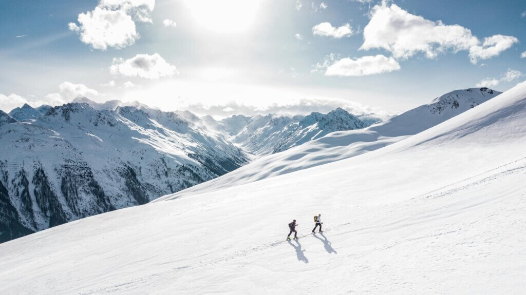 Two skiers climbing a sunlit snowy mountain slope in Ischgl, Austria, during winter.